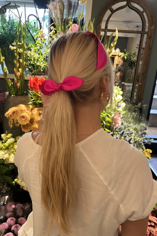 girl with blonde hair in pony tail wearing a fuchsia pink hair bow and headband